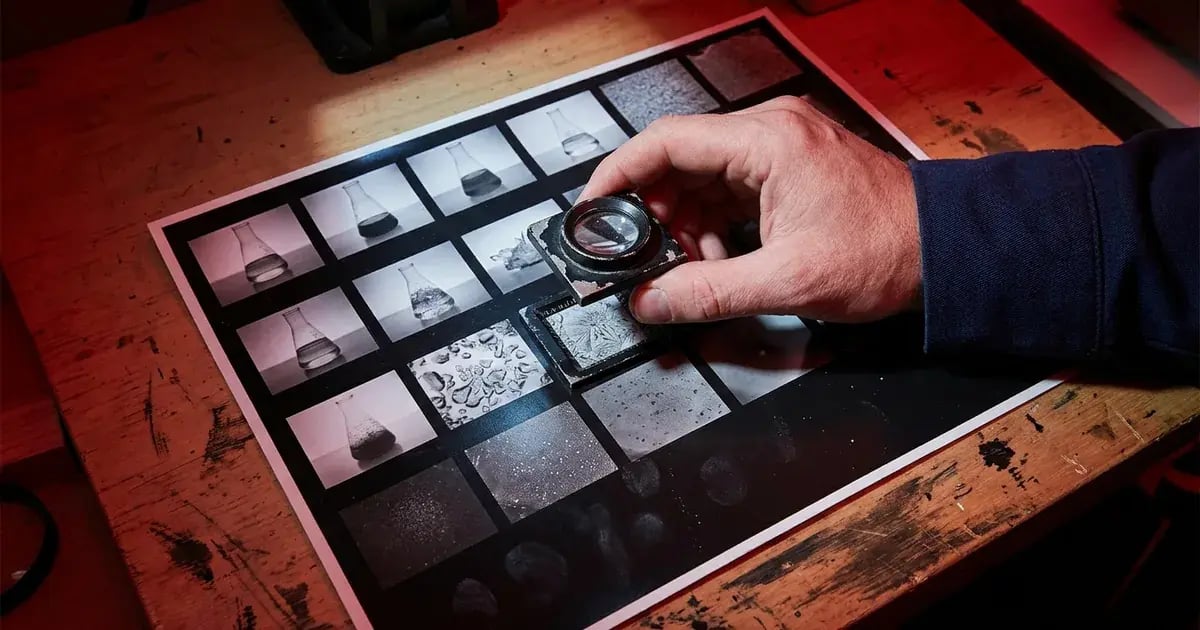 A hand using a loupe to find one useful frame on an analog photographic contact sheet