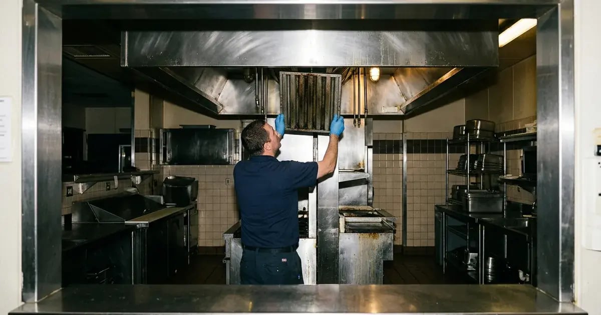 Service technician slides a grease-darkened baffle filter from a commercial kitchen exhaust hood.