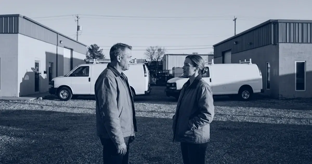 Two owners of neighboring small companies talk in a parking lot between their two buildings at the end of the workday.
