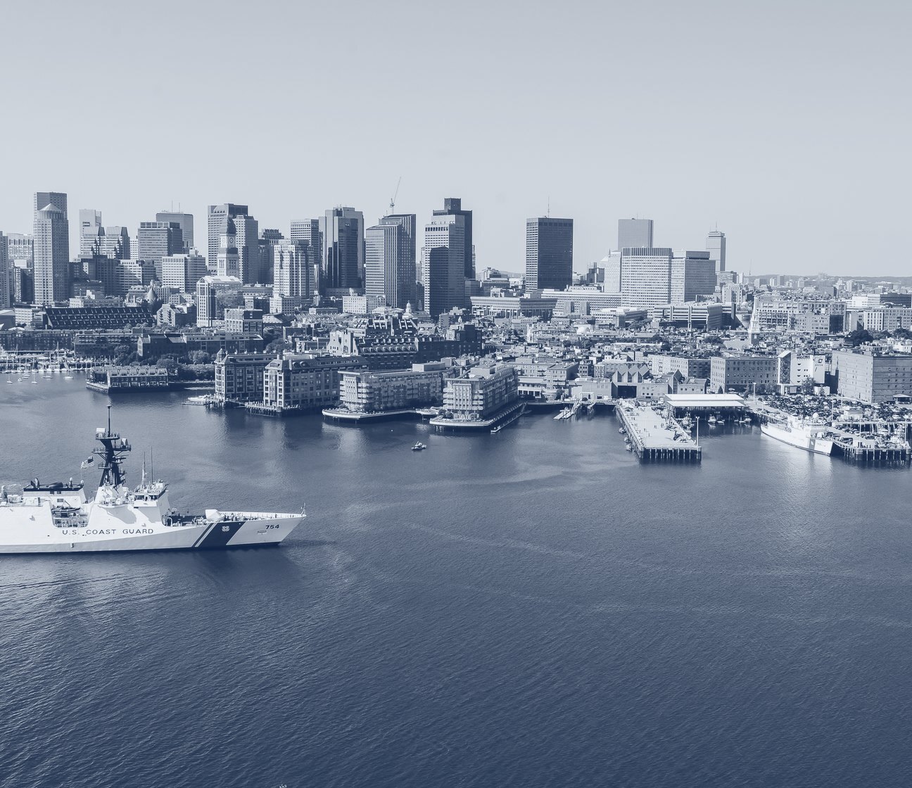 The Boston skyline across the harbor, with a Coast Guard cutter in the foreground.