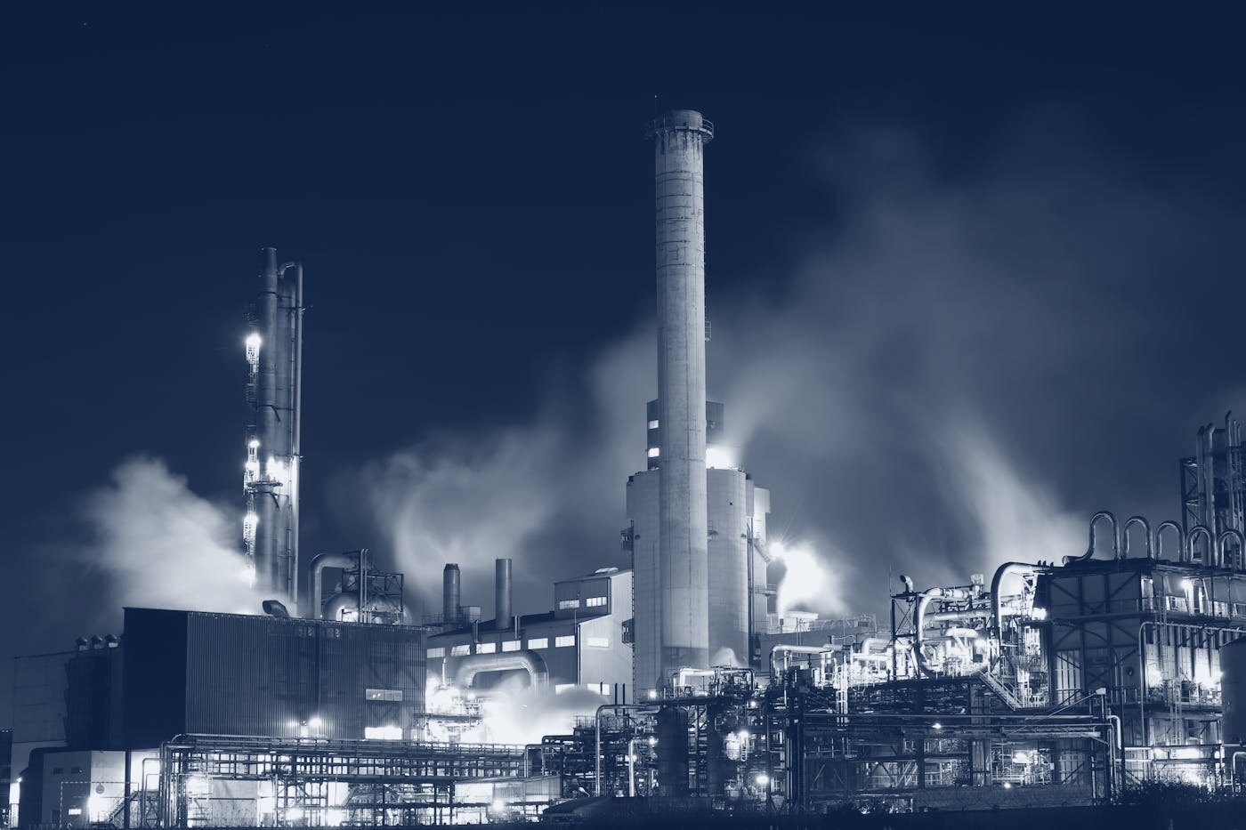 A process plant lit at night, rendered in navy tones.
