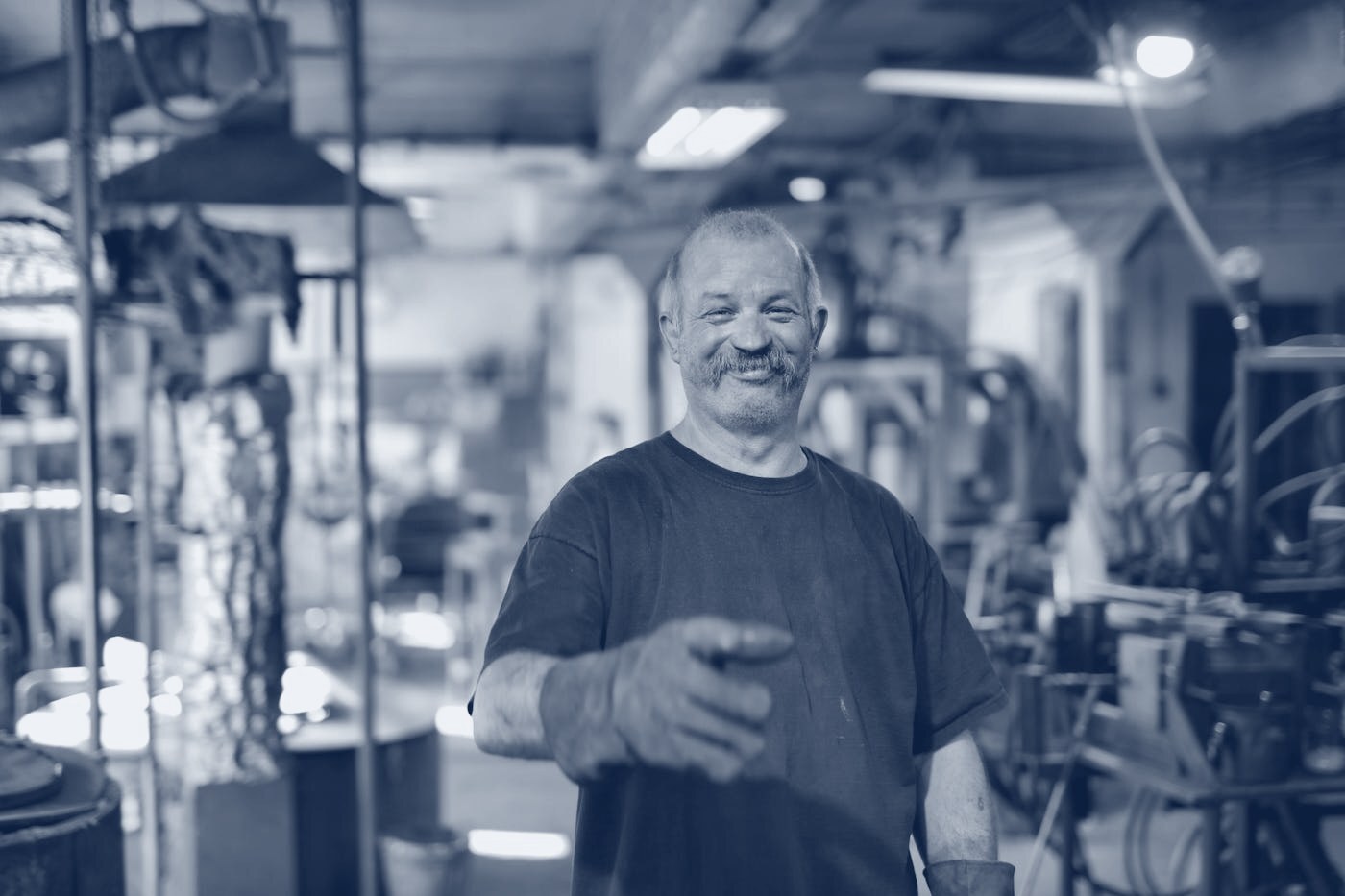 A fabricator working at a metal-cutting station on a manufacturing shop floor, shown in navy tones